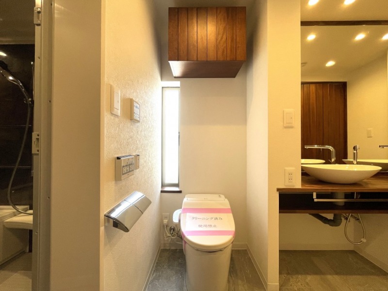 【洗面室のトイレ】窓があり明るいトイレです。タンクレスですっきりとしたデザインのウォシュレット付きトイレです。吊戸棚も設置されており、トイレットペーパーなどの消耗品の収納ができます。