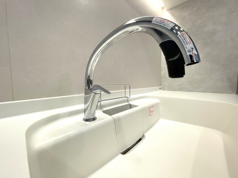 【キッチン：水栓】INAX製タッチレス水栓ナビッシュハンズフリーが設置されていています。人気の浄水器一体型のスワンネック水栓で、手やモノを感知して吐水と止水がタッチレスセンサーで触れずに行え、衛生的です。ワンアクションで吐水や混水、浄水と原水、シャワーの切り替えも可能で機能性と使いやすさに優れています。ハンドル位置にかかわらず水だけを吐水するエコセンサーと温度の変化が光の色の変化で一目でわかるルミナスサインも付いており、デザインだけでなく大きな洗い物もしやすく、お掃除楽々台座や蛇口部分がホースのように伸ばせるタイプでシンクも洗いやすい構造です。また省エネで節水もできます。