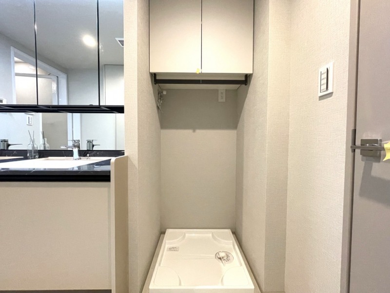 【洗面室：洗濯置場】洗面台横には洗濯機置き場があり、防水パンと洗濯機専用水栓・コンセント差し込み口が設置され、上部には洗剤やシャンプーストックなどが収納できる吊戸棚も備えてあります。