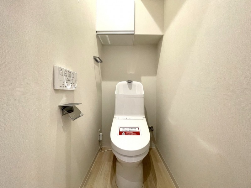 【トイレ】すっきりとしたデザインで清潔感があり、落ち着ける空間です。トイレもうれしいウォシュレット機能付きです。吊戸棚も設置されており、トイレットペーパーなどが収納できます。
