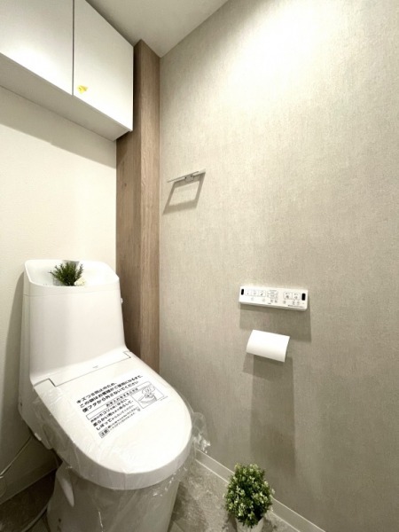 【トイレ】すっきりとしたデザインで清潔感があり、落ち着ける空間です。トイレもうれしいウォシュレット機能付きです。吊戸棚も設置されており、トイレットペーパーなどが収納できます。