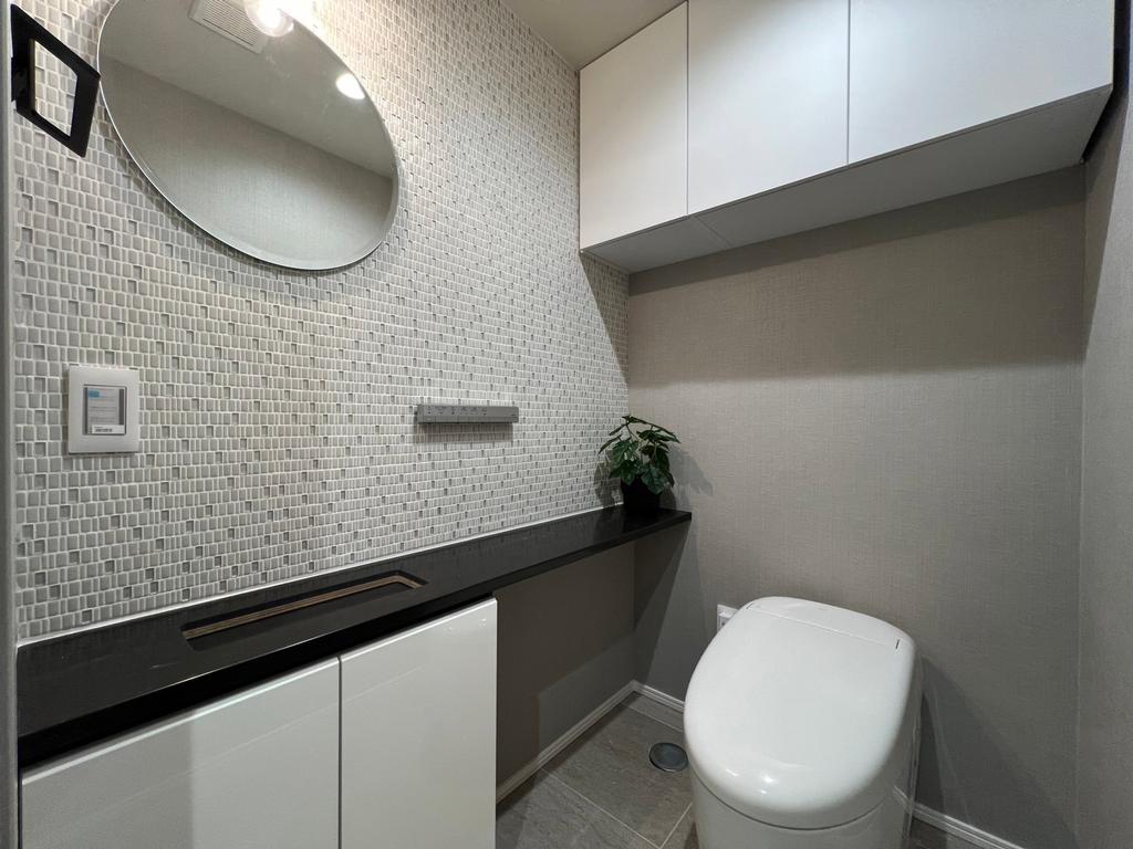 【トイレ】タンクレスのすっきりとしたデザインのウォシュレット付きトイレで、室内は一面のタイル貼りがスタイリッシュで、落ち着く上質な空間です。吊戸棚も設置されており、トイレットペーパーなどの消耗品の収納ができます。おしゃれな円形のミラー付の便利な専用手洗いスペースも付いています。