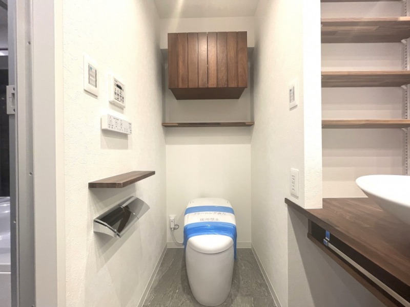 【洗面室横トイレ】トイレは、タンクレスですっきりとしたデザインのウォシュレット付きです。上部には吊戸棚も設置されています。