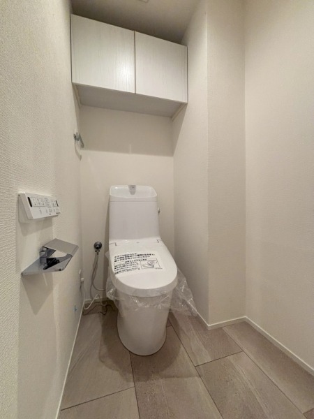 【トイレ】すっきりとしたデザインで清潔感があり、落ち着ける空間です。トイレもうれしいウォシュレット機能付きです。吊戸棚も設置されており、トイレットペーパーなどが収納できます。