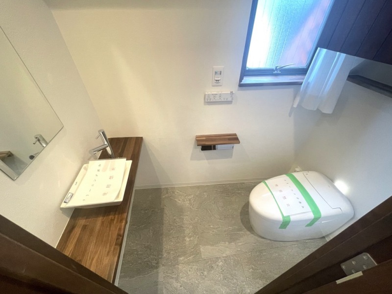 【トイレ】タンクレスですっきりとしたデザインのウォシュレット付きトイレです。室内は天然無垢材の温もりを感じる落ち着いた上質な空間です。吊棚も設置されており、トイレットペーパーなどの消耗品の収納ができます。ミラー付の便利な専用手洗いスペースも付いています。また窓があるので明るく、こもりがちな臭いも換気ができて快適です。