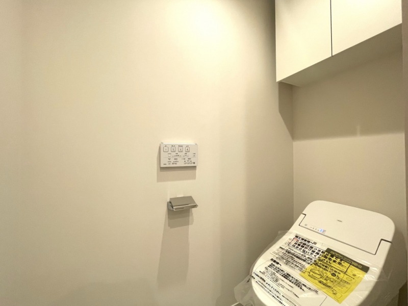 【洗面横トイレ】タンクレスですっきりとしたデザインのウォシュレット付きトイレが洗面室奥にあります。吊戸棚も設置されており、トイレットペーパーなどの消耗品の収納ができます。