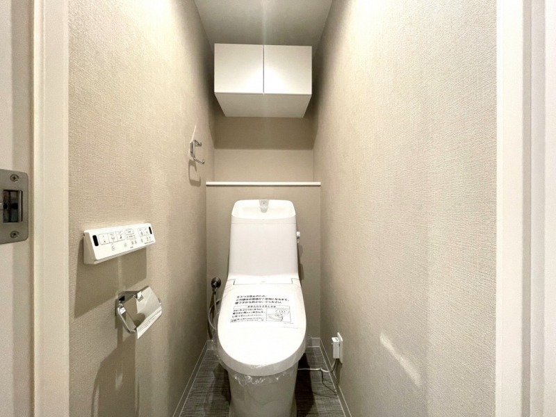 【トイレ】すっきりとしたデザインで清潔感があり、落ち着ける空間です。トイレもうれしいウォシュレット機能付きです。吊戸棚も設置されており、トイレットペーパーなどが収納できます。