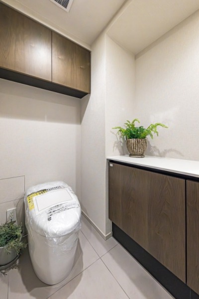 【トイレ】タンクレスのすっきりとしたデザインのウォシュレット付きトイレで、室内はシックに纏められた落ち着く上質な空間です。吊戸棚も設置されており、トイレットペーパーなどの消耗品の収納ができます。便利な専用手洗いスペースも付いています。
