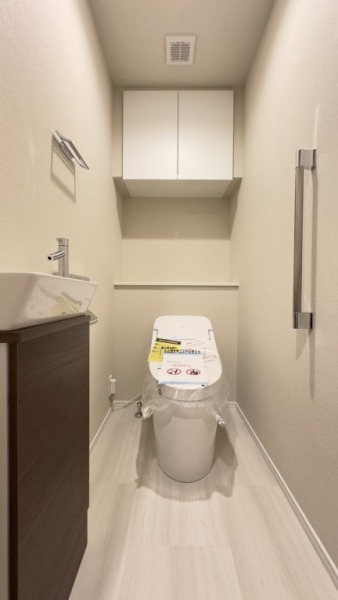 【トイレ】タンクレスのすっきりとしたデザインのウォシュレット付きトイレで、室内は清潔感があり落ち着く上質な空間です。吊戸棚も設置されており、トイレットペーパーなどの消耗品の収納ができます。便利な専用手洗いスペースも付いています。