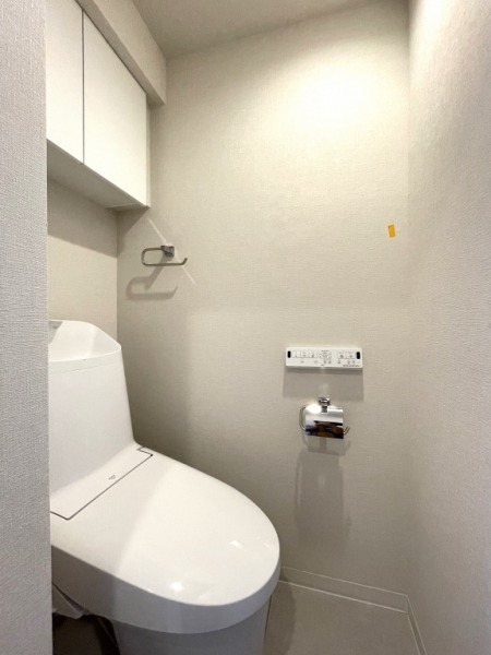 【トイレ】すっきりとしたデザインで清潔感があり、落ち着ける空間です。トイレもうれしいウォシュレット機能付きです。吊戸棚も設置されており、トイレットペーパーなどが収納できます。