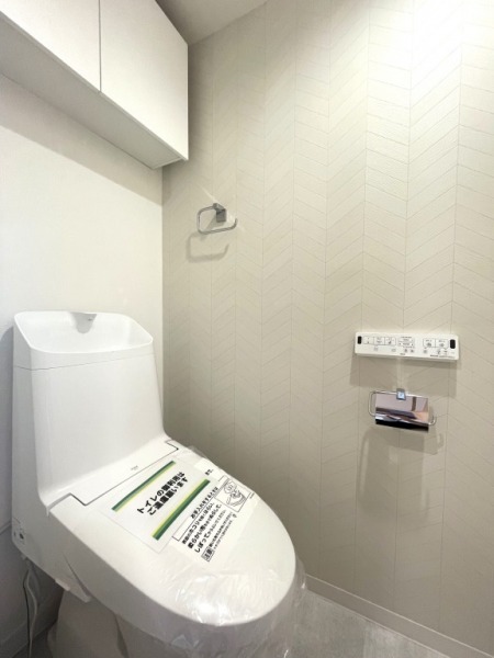 【トイレ】すっきりとしたデザインで清潔感があり、落ち着ける空間です。トイレもうれしいウォシュレット機能付きです。吊戸棚も設置されており、トイレットペーパーなどが収納できます。