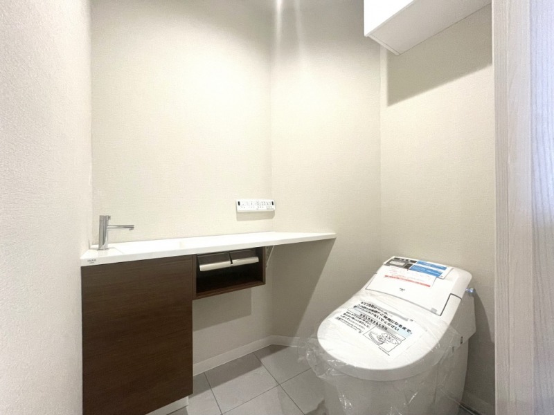 【トイレ】タンクレスのすっきりとしたデザインのウォシュレット付きトイレで、室内は清潔感があり落ち着く上質な空間です。吊戸棚も設置されており、トイレットペーパーなどの消耗品の収納ができます。便利な専用手洗いスペースも設けられています。