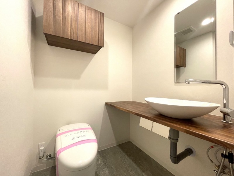 【トイレ】タンクレスのすっきりとしたデザインのウォシュレット付きトイレで、室内は清潔感があり落ち着く上質な空間です。吊戸棚も設置されており、トイレットペーパーなどの消耗品の収納ができます。ミラー付きの便利な専用手洗いスペースも設けられています。