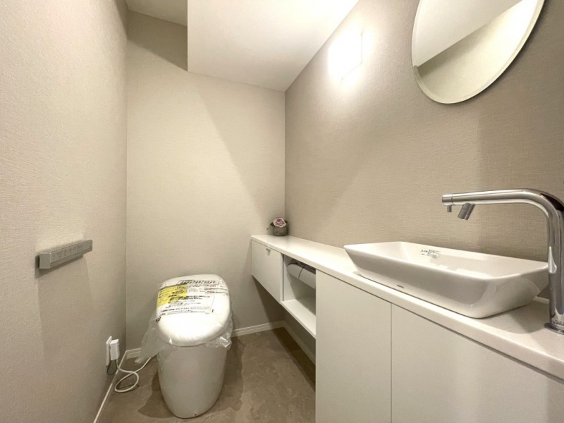 【トイレ:施工事例】タンクレスのすっきりとしたデザインのウォシュレット付きトイレで、室内は清潔感があり落ち着く上質な空間です。便利な専用手洗いスペースも設けられています。