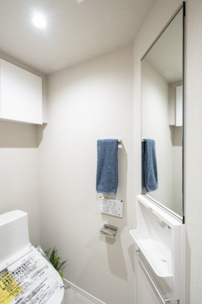 【トイレ】すっきりとしたデザインで清潔感があり、落ち着ける空間です。トイレもうれしいウォシュレット機能付きです。吊戸棚も設置されており、トイレットペーパーなどが収納できます。ミラー付きの便利な専用手洗いスペースも設けられています。