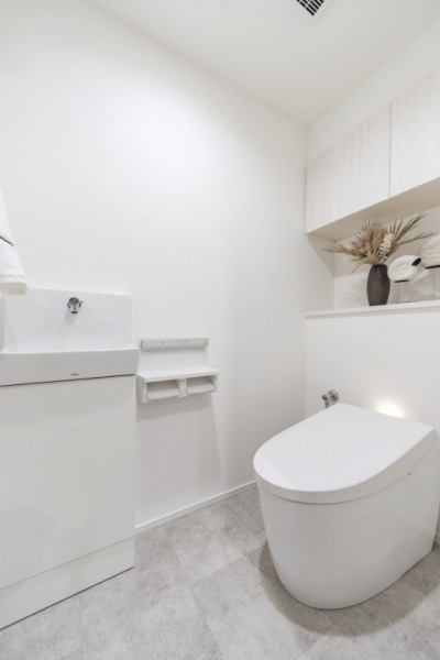 【トイレ】タンクレスのすっきりとしたデザインのウォシュレット付きトイレで、室内はホワイトベースで清潔感があり落ち着く上質な空間です。吊戸棚も設置されており、トイレットペーパーなどの消耗品の収納ができます。便利な専用手洗いスペースも設けられています。