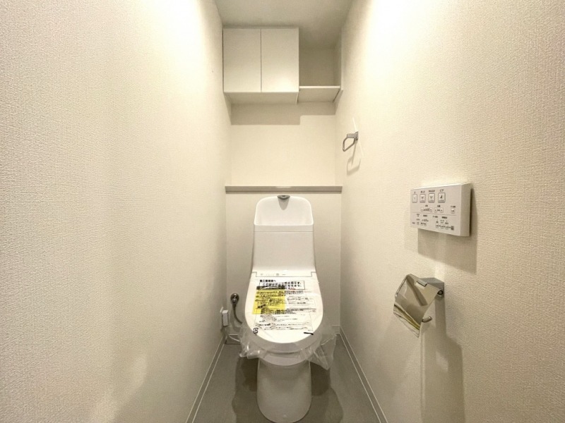 【トイレ】すっきりとしたデザインで清潔感があり、落ち着ける空間です。トイレもうれしいウォシュレット機能付きです。吊戸棚も設置されており、トイレットペーパーなどが収納できます。