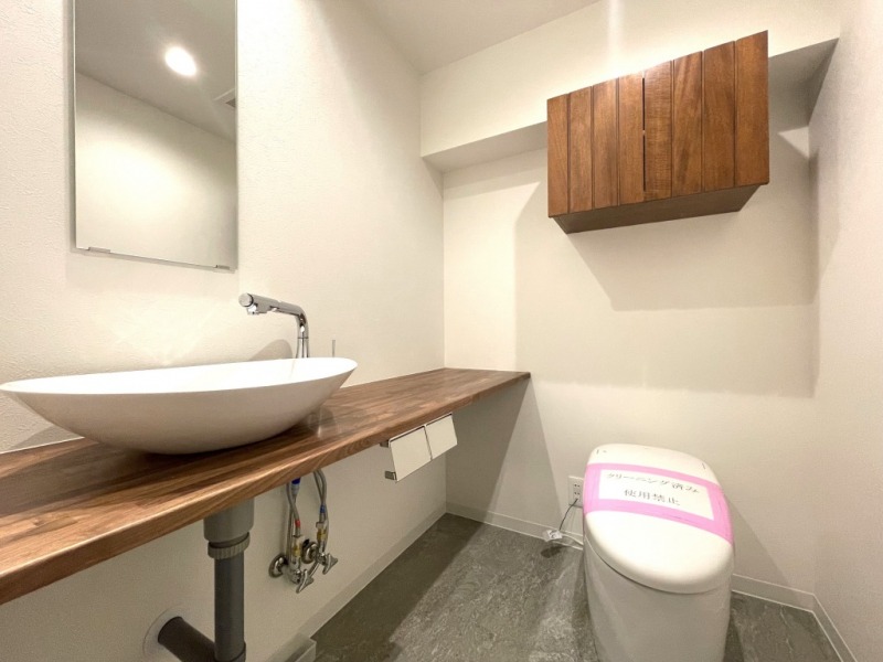 【トイレ】タンクレスですっきりとしたデザインのウォシュレット付きトイレです。室内は天然無垢材の温もりを感じる落ち着いた上質な空間です。吊戸棚も設置されており、トイレットペーパーなどの消耗品の収納ができます。ミラー付の便利な専用手洗いスペースが設けられています。