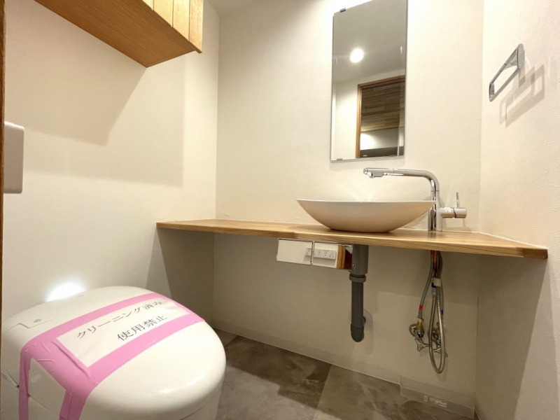 【トイレ】タンクレスですっきりとしたデザインのウォシュレット付きトイレです。室内は天然無垢材の温もりを感じる落ち着いた上質な空間です。吊戸棚も設置されており、トイレットペーパーなどの消耗品の収納ができます。ミラー付の便利な専用手洗いスペースが設けられています。