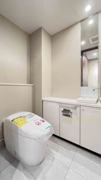 【トイレ】洋室側のトイレです。タンクレスのすっきりとしたデザインのウォシュレット付きトイレで、室内は清潔感があり、明るい色味の落ち着く上質な空間です。ミラー付きの便利な専用手洗いスペースも設けられています。