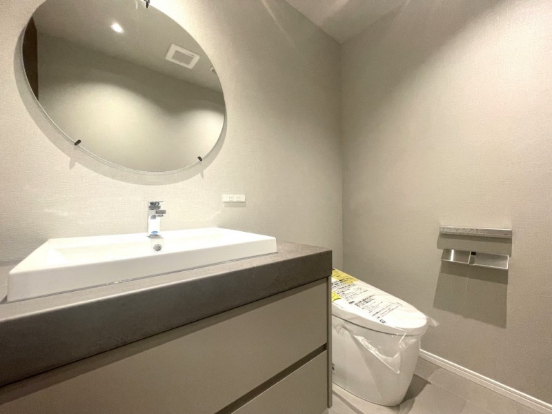 【トイレ】タンクレスのすっきりとしたデザインのウォシュレット付きトイレで、室内は清潔感があり落ち着く上質な空間です。おしゃれな円形ミラーが付いた、収納付き洗面台が設けられています。