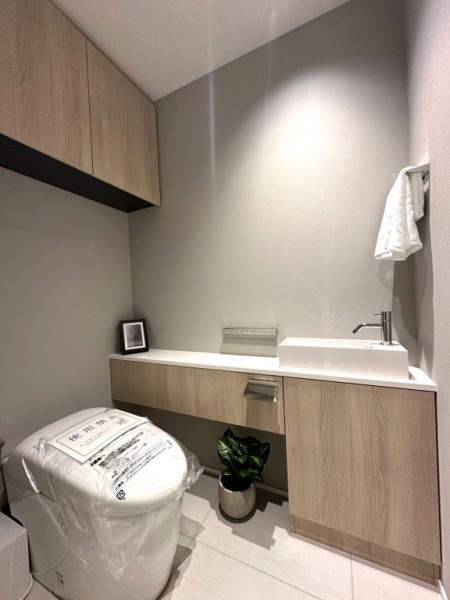 【トイレ】タンクレスのすっきりとしたデザインのウォシュレット付きトイレで、室内は清潔感があり落ち着く上質な空間です。カウンターや吊戸棚も設置されており、トイレットペーパーなどの消耗品の収納ができます。便利な専用手洗いスペースも設けられています。