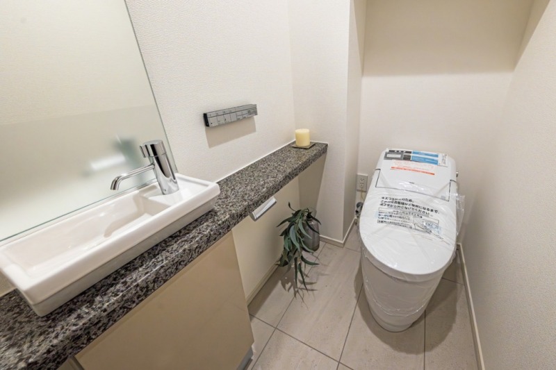 【トイレ】タンクレスのすっきりとしたデザインのウォシュレット付きトイレで、室内は清潔感があり落ち着く上質な空間です。ミラー付きの便利な専用手洗いスペースも設けられています。
