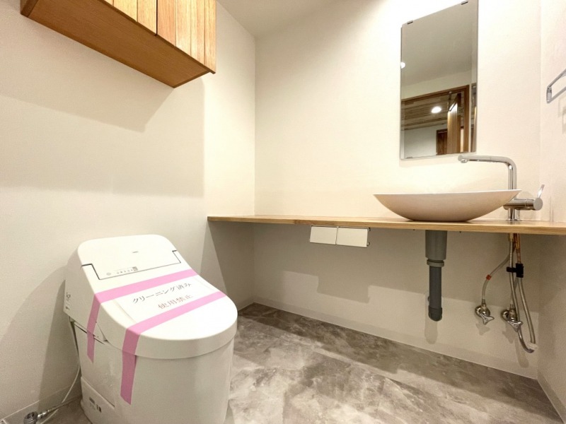 【トイレ】トイレは、タンクレスですっきりとしたデザインのウォシュレット付きトイレです。室内は天然無垢材の温もりを感じる落ち着いた上質な空間です。吊戸棚も設置されており、トイレットペーパーなどの消耗品の収納ができます。ミラー付の便利な専用手洗いスペースが設けられています。