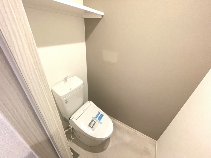【トイレ】すっきりとしたデザインで清潔感があり、落ち着ける空間です。トイレもうれしいウォシュレット機能付きです。吊戸棚も設置されており、トイレットペーパーなどが収納できます。