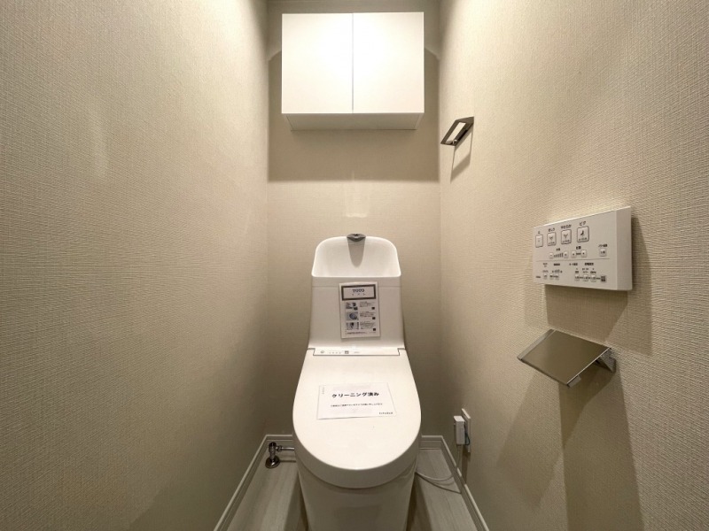 【トイレ】すっきりとしたデザインで清潔感があり、落ち着ける空間です。トイレもうれしいウォシュレット機能付きです。吊戸棚も設置されており、トイレットペーパーなどが収納できます。