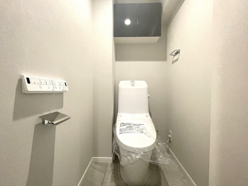 【トイレ】すっきりとしたデザインで清潔感があり、落ち着ける空間です。トイレもうれしいウォシュレット機能付きです。吊戸棚も設置されており、トイレットペーパーなどが収納できます。