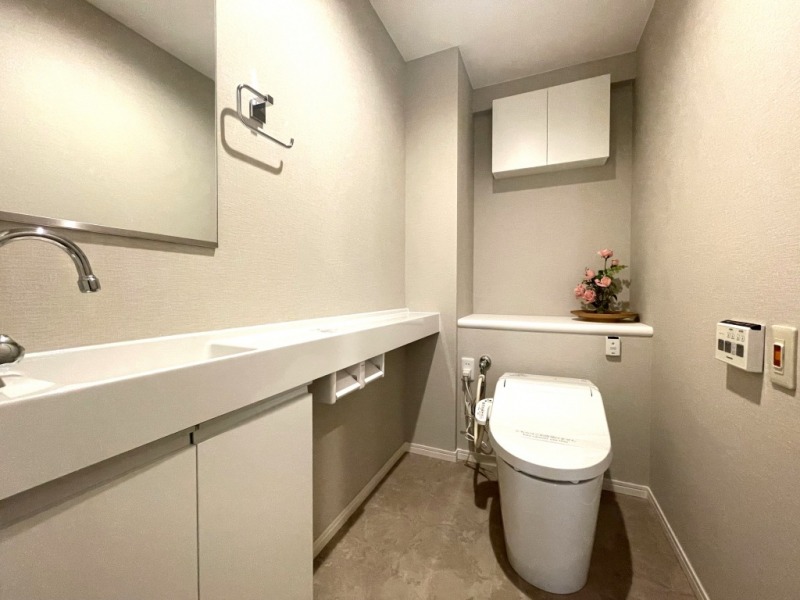 【トイレ】タンクレスでお手入れもしやすいすっきりとしたデザインの洗浄付きトイレで、室内は清潔感があり落ち着く上質な空間です。吊戸棚も設置されており、トイレットペーパーやタオルなどの収納ができます。ミラー付きの便利な専用手洗いスペースも設けられています。