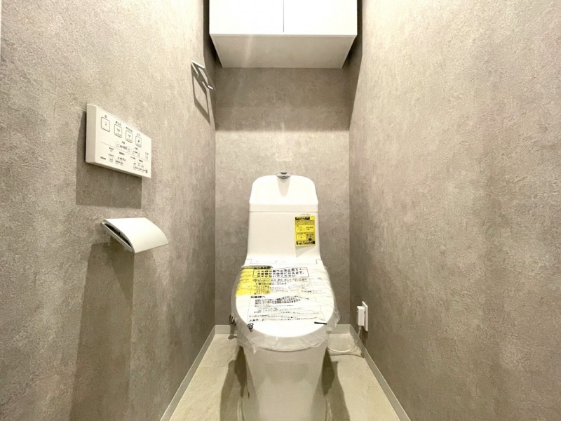 【トイレ】すっきりとしたデザインで清潔感があり、シックで落ち着ける空間です。トイレもうれしい洗浄機能付きです。吊戸棚も設置されており、トイレットペーパーなどが収納できます。
