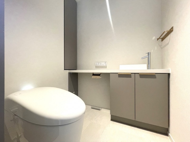 【トイレ】タンクレスのすっきりとしたデザインの汚れもつきにくい洗浄付きトイレで、室内は清潔感があり落ち着くシックで上質な空間です。便利な専用手洗いスペースも設けられています。真鍮色の金具がアクセントになっています。