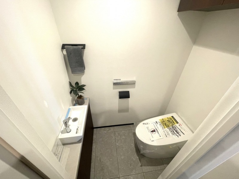 【トイレ】タンクレスのすっきりとしたデザインの汚れもつきにくい洗浄付きトイレで、室内は清潔感があり落ち着く上質な空間です。吊戸棚も設置されており、トイレットペーパーやタオルなどの収納ができます。便利な専用手洗いスペースも設けられています。