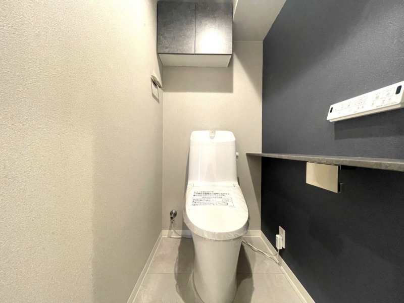 【トイレ】すっきりとしたシックなデザインで清潔感があり、落ち着ける空間です。トイレもうれしい洗浄機能付きです。吊戸棚も設置されており、トイレットペーパーなどが収納できます。