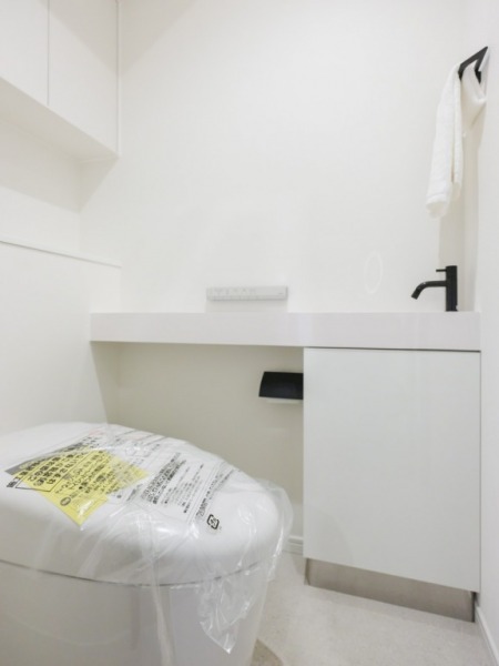 【トイレ】タンクレスのすっきりとしたデザインの汚れもつきにくいウォシュレット付きトイレで、室内はホワイトを基調とし、清潔感がある落ち着く空間です。吊戸棚も設置されており、トイレットペーパーやタオルなどの収納ができます。便利な専用手洗いスペースも設けられています。