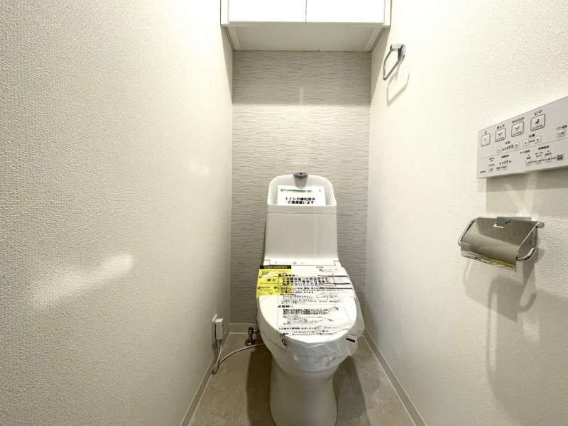 【トイレ】すっきりとしたデザインで清潔感があり、落ち着ける空間です。トイレもうれしい洗浄機能付きです。吊戸棚も設置されており、トイレットペーパーなどが収納できます。