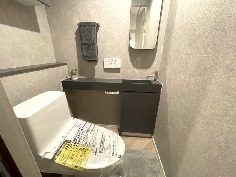 【トイレ】シックなデザインで、落ち着ける空間です。トイレもうれしい洗浄機能付きです。吊戸棚も設置されており、トイレットペーパーなどが収納できます。ミラー付きの便利な専用手洗いスペースも設けられています。