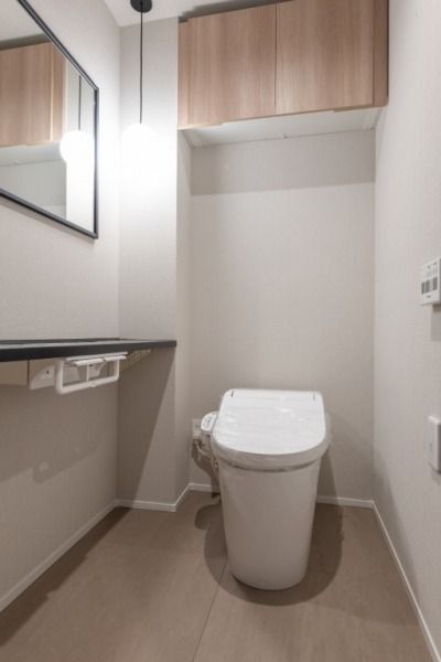 【トイレ】タンクレスでお手入れもしやすいすっきりとしたデザインの洗浄付きトイレで、室内は清潔感があり落ち着く上質な空間です。吊戸棚も設置されており、トイレットペーパーやタオルなどの収納ができます。ミラー付きの便利な専用手洗いスペースも設けられています。