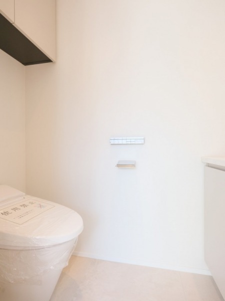 【トイレ】タンクレスのすっきりとしたデザインの汚れもつきにくい洗浄機能付きトイレで、室内はホワイトを基調とし、清潔感のある落ち着く空間です。吊戸棚も設置されており、トイレットペーパーやタオルなどの収納ができます。便利な専用手洗いスペースも設けられています。