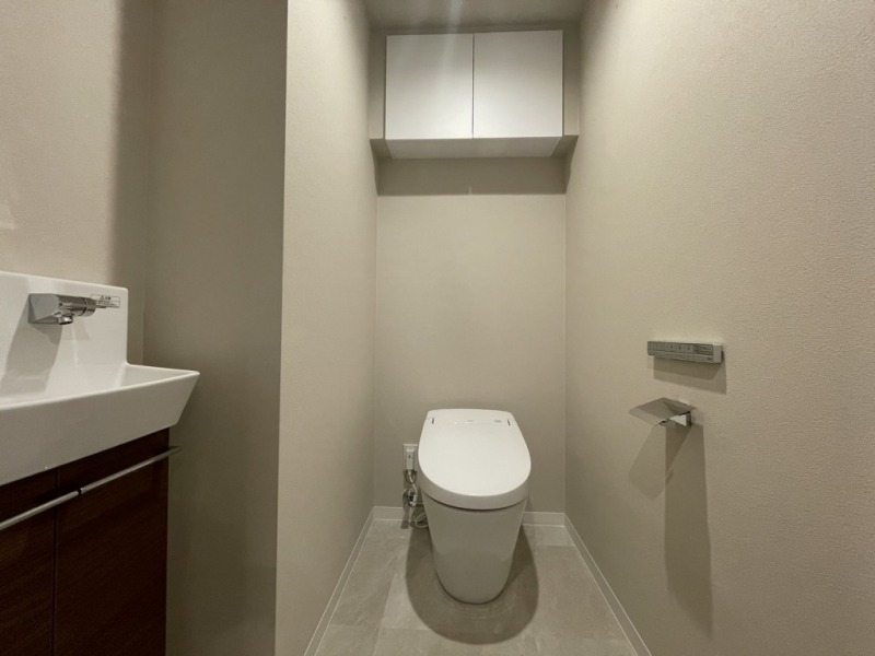 【トイレ】タンクレスでお手入れもしやすいすっきりとしたデザインの洗浄付きトイレで、室内は清潔感があり落ち着く上質な空間です。吊戸棚も設置されており、トイレットペーパーやタオルなどの収納ができます。便利な専用手洗いスペースも設けられています。