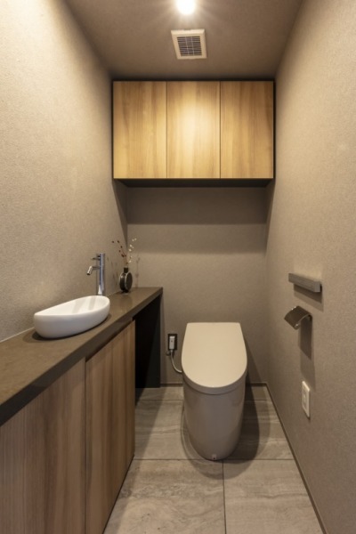 【トイレ】タンクレスの温水洗浄機能付きトイレで、お手入れもしやすくすっきりしていて、室内は木の温もりを感じる落ち着く上質な空間です。吊戸棚も設置されており、トイレットペーパーやタオルなどの収納ができます。便利な専用手洗いスペースも設けられています。