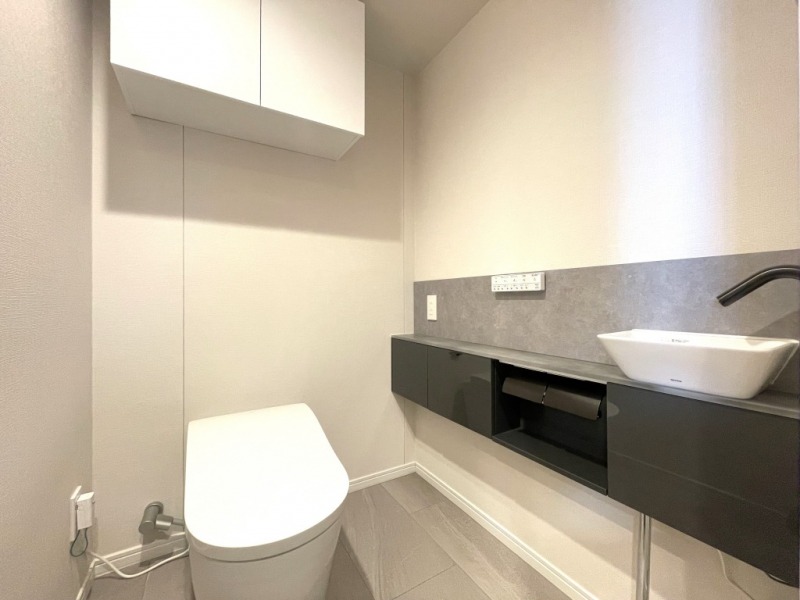 【トイレ】タンクレスの温水洗浄機能付きトイレで、お手入れもしやすくすっきりしていて、室内は清潔感があり落ち着く上質な空間です。吊戸棚も設置されており、トイレットペーパーやタオルなどの収納ができます。便利な専用手洗いスペースも設けられています。