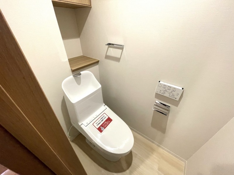 【トイレ】すっきりとしたデザインで清潔感があり、落ち着ける空間です。トイレもうれしい洗浄機能付きです。吊戸棚も設置されており、トイレットペーパーなどが収納できます。