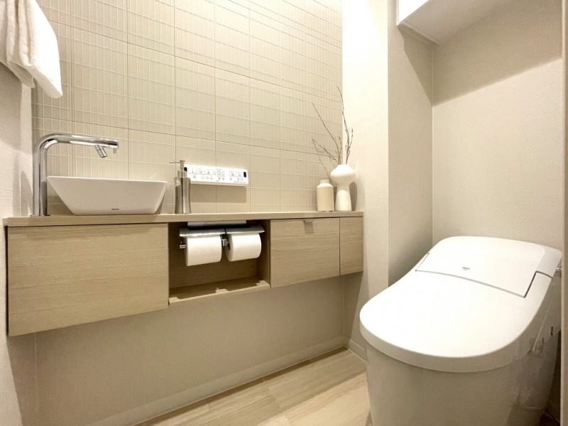 【トイレ】タンクレスの温水洗浄機能付きトイレで、お手入れもしやすくすっきりしていて、室内は清潔感があり落ち着く上質な空間です。吊戸棚も設置されており、トイレットペーパーやタオルなどの収納ができます。便利な専用手洗いスペースも設けられています。