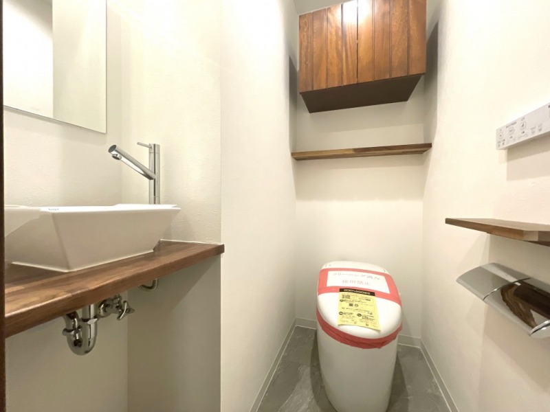【トイレ】タンクレスですっきりとしたデザインのウォシュレット付きトイレです。室内は天然無垢材の温もりを感じる落ち着いた上質な空間です。吊戸棚も設置されており、トイレットペーパーなどの消耗品の収納ができます。ミラー付の便利な専用手洗いスペースも付いています。