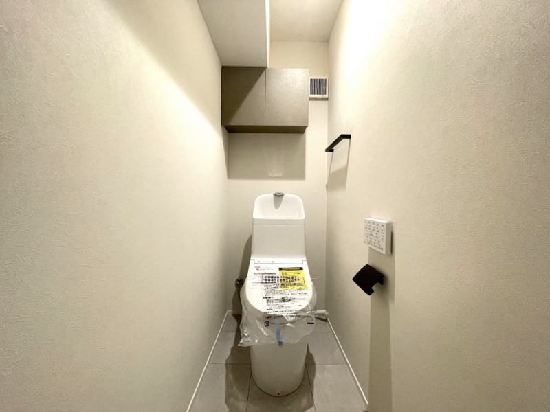 【トイレ】すっきりとしたデザインで清潔感があり、落ち着ける空間です。トイレもうれしい洗浄機能付きです。吊戸棚も設置されており、トイレットペーパーなどが収納できます。