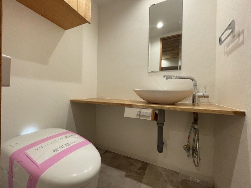 【トイレ:弊社施工事例】タンクレスの温水洗浄機能付きトイレで、お手入れもしやすくすっきりしています。室内は清潔感があり落ち着く上質な空間です。吊戸棚も設置されており、トイレットペーパーやタオルなどの収納ができます。便利な専用手洗いスペースも設けられています。