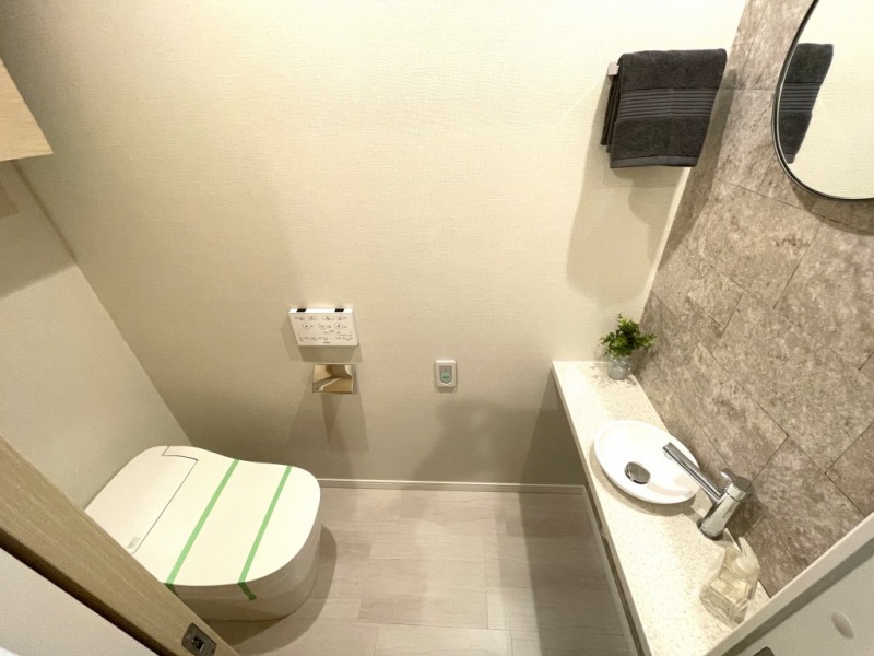 【トイレ】タンクレスですっきりとしたデザインでお手入れもしやすい温水洗浄機能付きトイレです。室内は清潔感があり落ち着く上質な空間です。トイレットペーパーなどが収納できる吊戸棚も設置され、カウンターやミラー付の便利な専用手洗いスペースも設けられています。